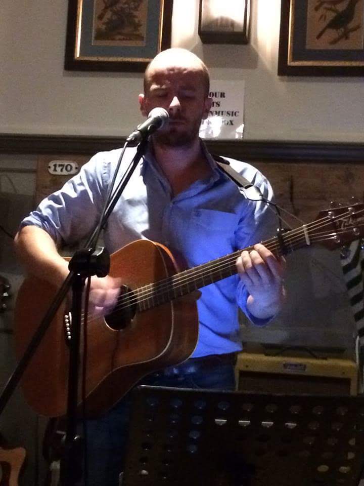 coloured picture of eoin standing up with a guitar facing the camera in a pub